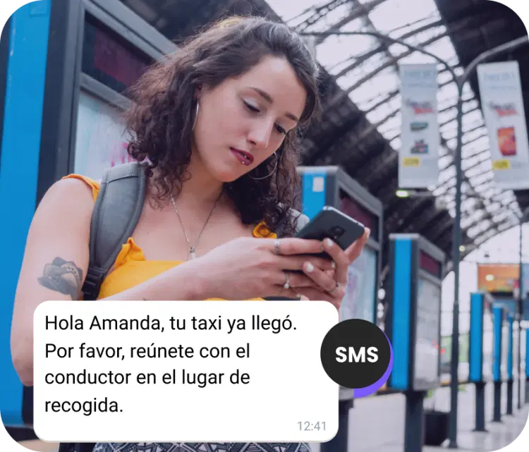 Chica con mochila en la estación revisando un SMS sobre la llegada de su taxi